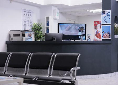 Clinic registration counter in waiting room lobby, computer to make checkup appointments with healthcare report papers. Empty hospital reception desk with medical forms and insurance support.